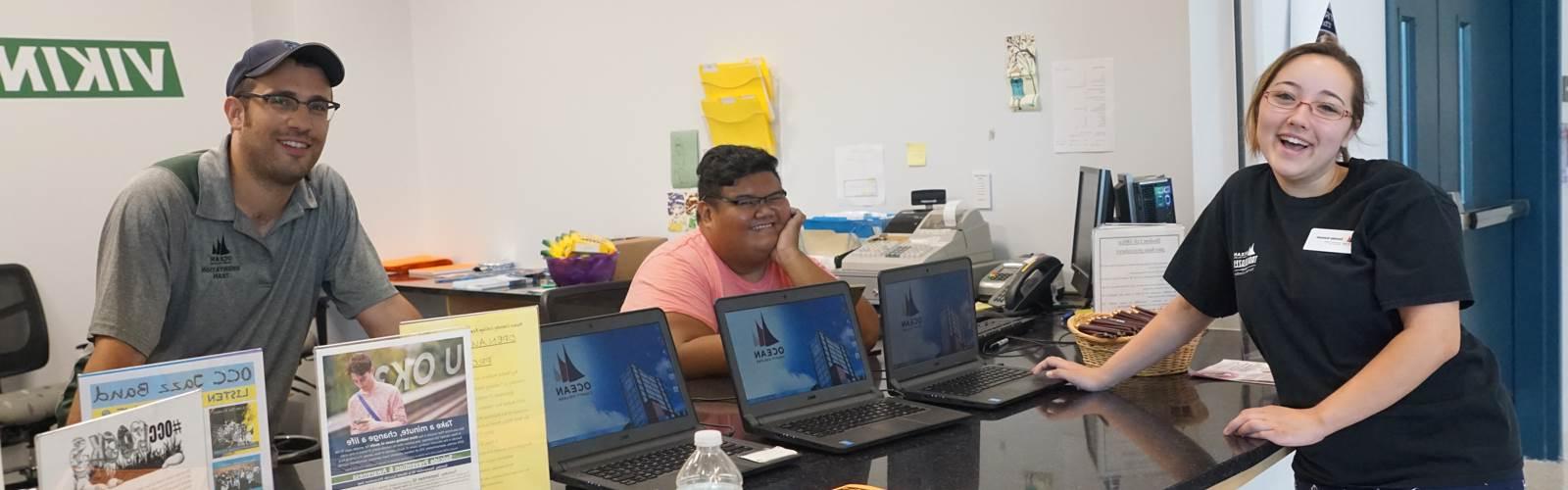 three students at computers smiling at the camera